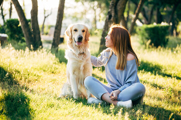 a young woman and a golden retriever dog sit on the grass in the park