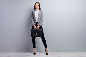 Full body photo of attractive lady smiling worker young promoted chief look interested side empty space hold diplomat wear specs shirt blazer pants high-heels isolated grey color background