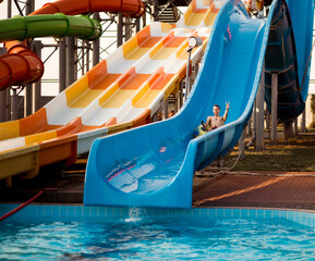 Happy young man has active summer vacation activities and ride on water slide at the water park.