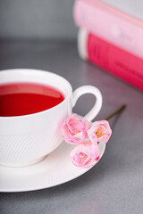 Raspberry tea, pink freesia flowers and books on a gray background
