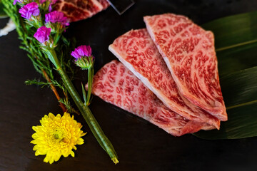 Slice Japanese beef neck chuck or jyu rosu wagyu serving on black plate and decorate with flower. Preparation for BBQ.