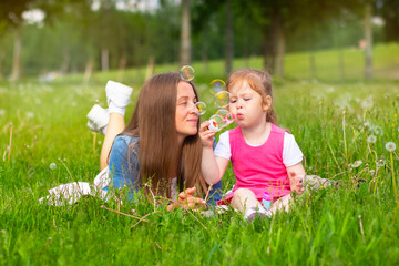 Fototapeta premium Happy mom with daughter play with soapy bubble in the park on green grass. Little girl and woman are walking.
