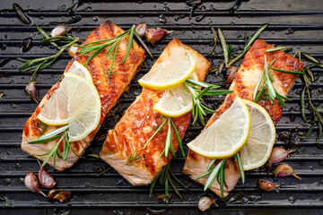 Grilled salmon fillets sprinkled with fresh herbs and lemon juice on a grill plate close up 