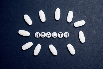 Health sign made from beads on a dark blue background with white pills around it, Health and medical treatment concept.