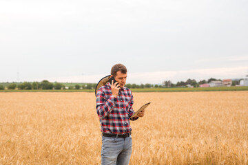 Naklejka na ściany i meble Caucasian farmer checking wheat field progress with tablet using internet. Agriculture and harvesting concept.