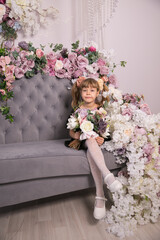 Pretty little girl holding a bunch of colouful flowers in her hands against a backdrop of closed curtains with copyspace