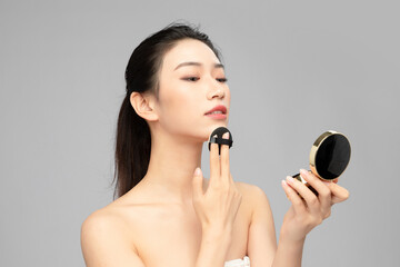Close-up face of beautiful Asian woman using compact powder on grey background