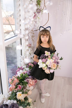 Beautiful little girl in black sleeveless top wearing a cat ear headband and holding a bunch of flowers