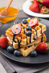 Fresh homemade food of berry Belgian waffles with honey, chocolate, strawberry, blueberry, maple syrup and cream. Healthy dessert breakfast concept with juice