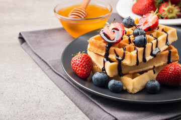 Fresh homemade food of berry Belgian waffles with honey, chocolate, strawberry, blueberry, maple syrup and cream. Healthy dessert breakfast concept with juice