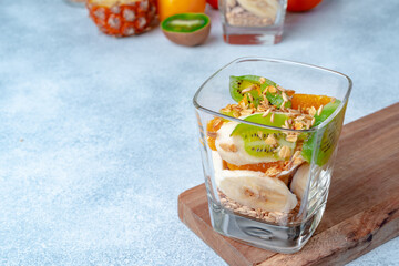 Glass with fruit pieces and oatmeal muesli on wooden board