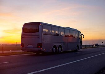 A large comfortable passenger bus against the orange sky with sunset rides on the highway. The concept of European passenger transportation in companies, e-ticket © HENADZY