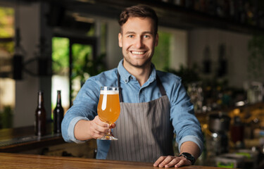 Fototapeta premium Craft beer. Smiling barman looks at camera and gives glass of drink