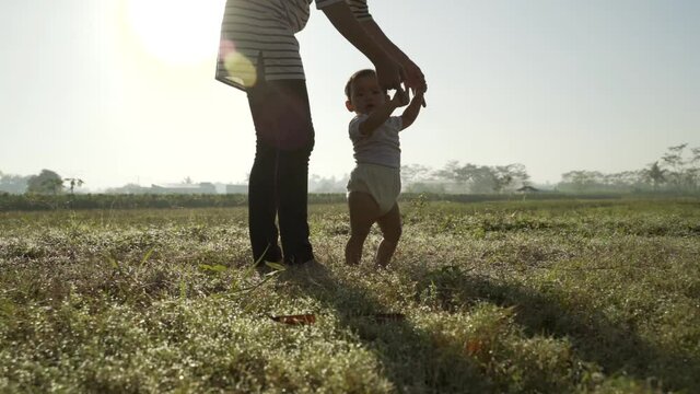 baby first step outdoor walking. mother help her baby to walk her first step in the field during sunset