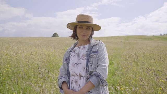 Slo mo video of Sincerely smiling young Woman dressed jeans jacket and light summer dress on the high green grass with wildflowers meadow. Human in the nature concept footage.