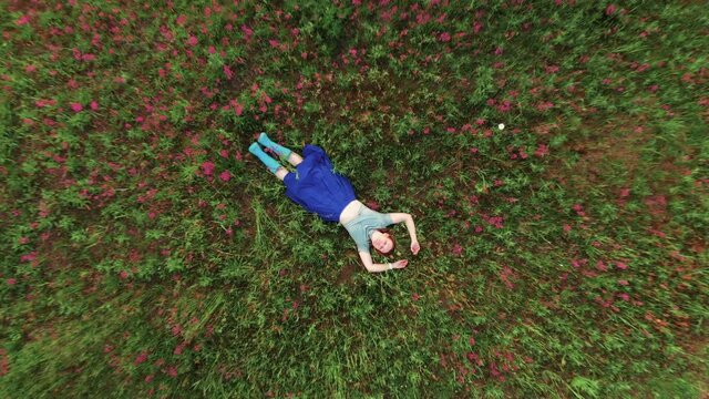 Staycation. 40 years old woman with arms and legs outstretched lying and similing on green grass in park meadow with red flowers. Beautiful summertime. Hello summer, spring and sport consept.