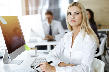 Blond business woman using computer at workplace in sunny office. Working for pleasure and success