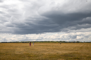 Naklejka na ściany i meble thunderclouds over the yellow field. two people are standing in a field.