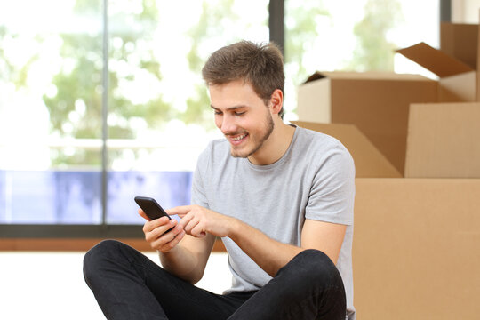 Happy man with boxes using phone moving home