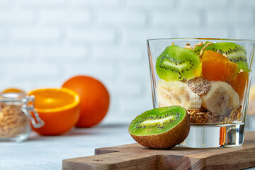 Glass with fruit pieces and oatmeal muesli on wooden board