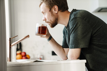 Photo of serious redhead man reading newspaper while drinking tea