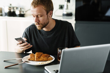 Fototapeta na wymiar Photo of man using laptop and cellphone while having breakfast