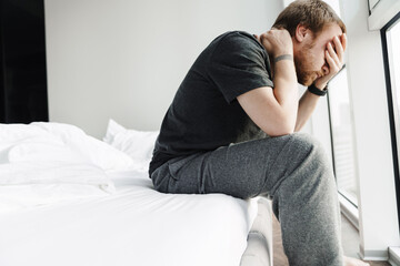 Fototapeta premium Photo of displeased redhead man covering his face while sitting on bed