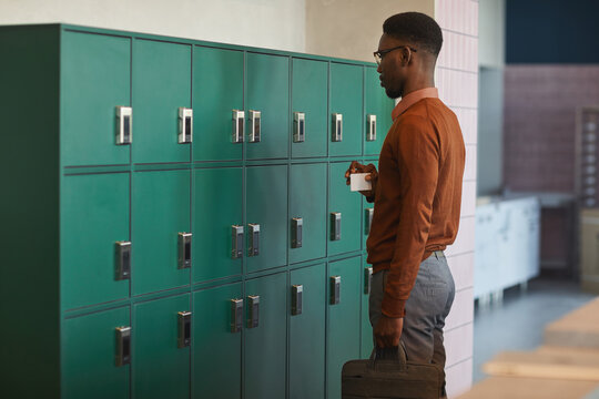 Portrait of young African-American man opening locker in college or office building, copy space