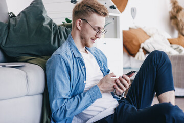 Obraz premium A young man at home with a mobile phone in his hands. Close-up of a young man using the phone at home. A man communicates with friends on a mobile phone. Young business man working from home 