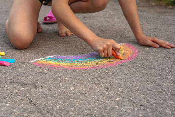 Little girl child draws a rainbow on the asphalt using crayons, world and social concept, place for text copy space