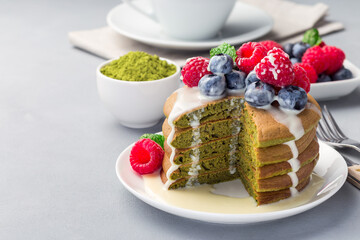Cuted stack of matcha pancakes served with condensed milk, blueberry and raspberry on white plate, horizontal, copy space