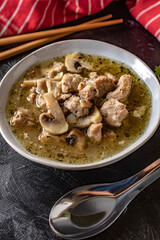 Soup with pieces of pork and mushrooms in bowl.