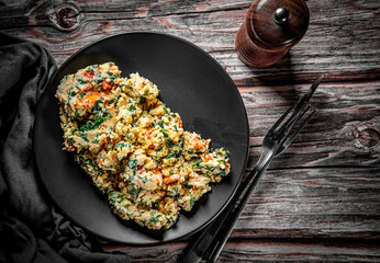scrambled eggs with spinach and tomato in plate on wooden table background
