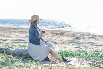 woman in a straw hat stands by the sea with a glass of wine, rear view
