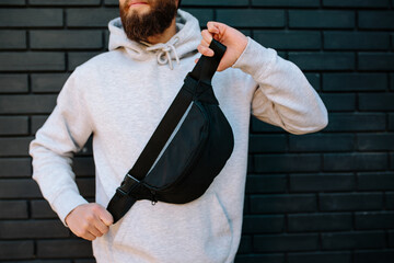Handsome hipster guy wearing gray blank hoodie, black cap and black waist bag with space for your...