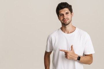 Portrait of pleased young man smiling and pointing finger aside