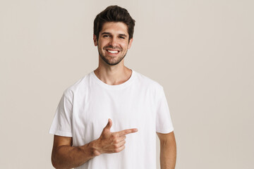 Portrait of joyful young man smiling and pointing finger aside