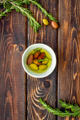 Olives in bowl near rosemary on wooden table top view copy space