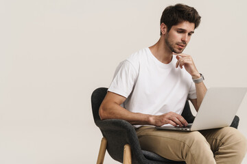 Portrait of thinking man working with laptop while sitting on armchair
