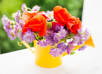 Beautiful bouquet of bright wildflowers in yellow watering can on window.