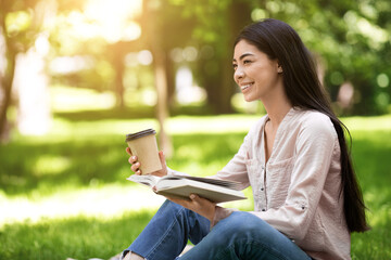 Obraz premium Young asian girl reading book and drinking takeaway coffee in park outdoors