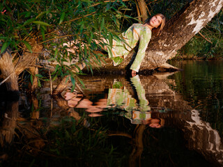 beautiful girl on a tree over water at sunset