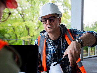 Fototapeta premium Concept of construction works. A man in a construction helmet on site sitting in front of a woman engineer and talks to her about the construction.