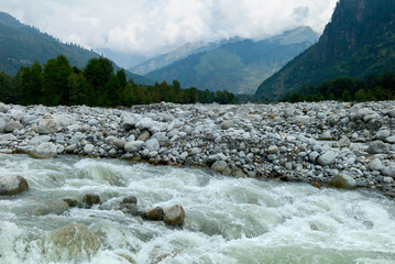 River flows through valley flanked by rocks in Manali, India.