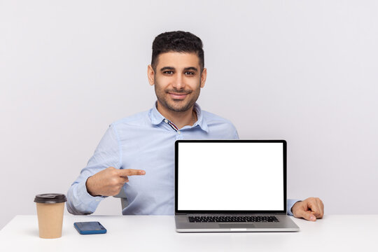 Look at advertisement! Happy elegant man employee sitting in office workplace, pointing laptop blank display, mock up empty place for website promotion. indoor studio shot isolated on white background