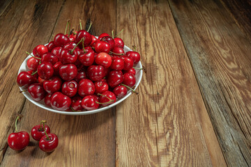 fresh, juicy cherries in a plate on a wooden table close-up, rustic style