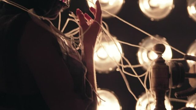 The girl is engaged in needlework on an old antique sewing machine. There are many lamps on the wall. Hands of a seamstress with threads closeup