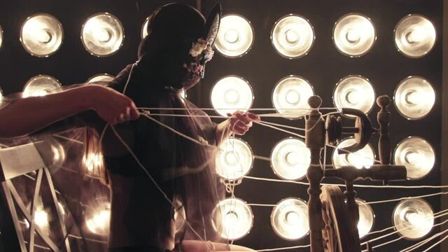 A girl in a mask works at a weaving table against a background of yellow lamps. Yarn and thread, handmade