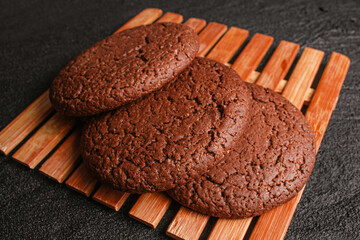 Three chocolate oatmeal cookies lie on a bamboo leaf on black concrete. flat lay top view