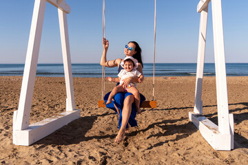 Beautiful woman swinging with her baby at the fine sandy Beach enjoying the idyllic scene of the...